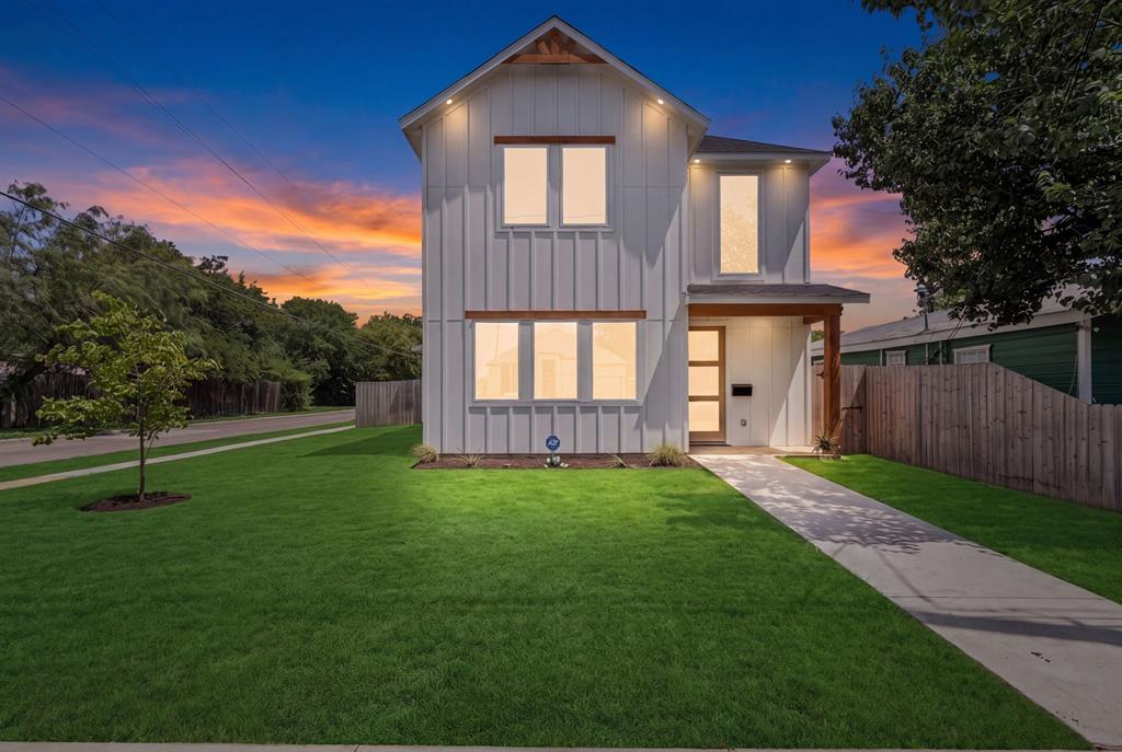 Modern farmhouse exterior featuring vertical board-and-batten siding, natural wood-finish accents, large multi-pane windows, recessed soffit lighting, and a concrete walkway