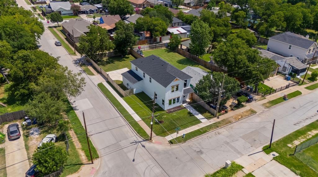 Corner lot property featuring a white vertical-siding exterior, dark shingled roof, concrete driveway, and expansive grass lawn