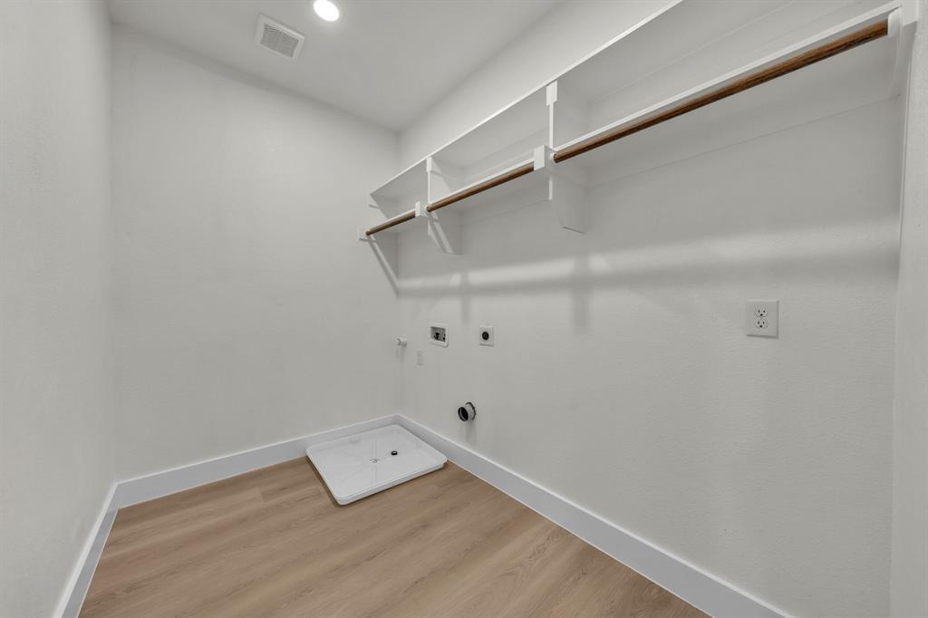 Utility room featuring wood-finish flooring, white shelving with an integrated clothes rod, and an appliance drain pan