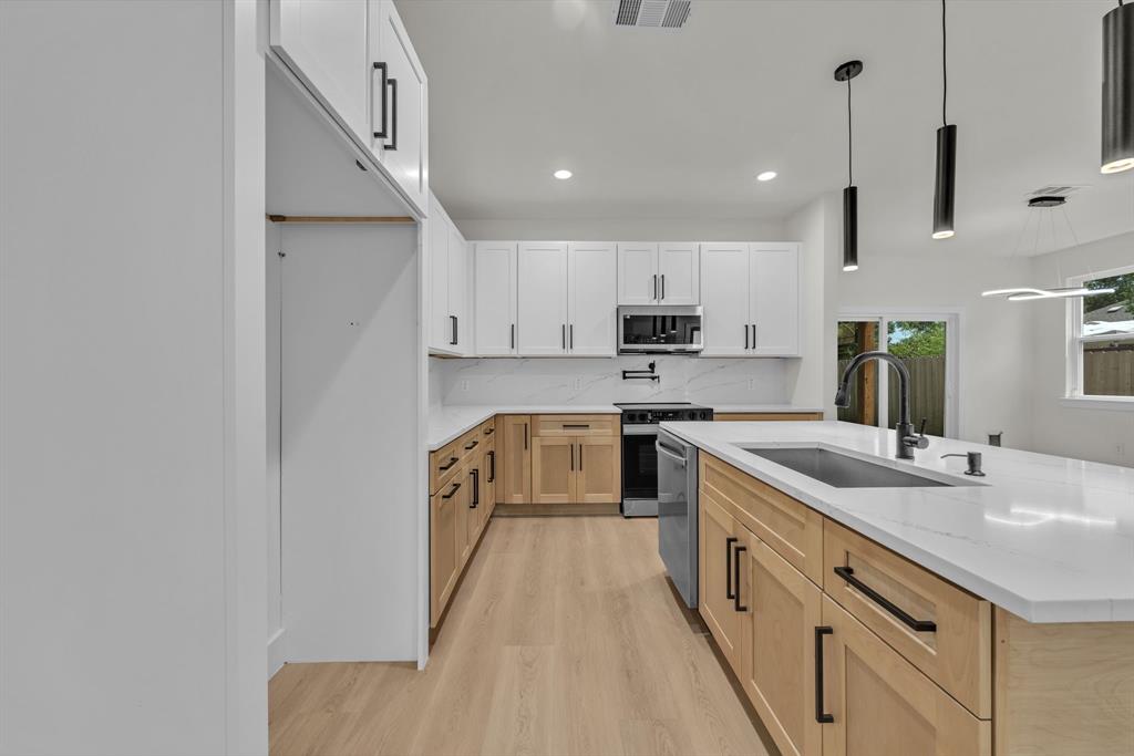 Kitchen featuring two-tone cabinetry with matte black hardware, quartz countertops, a central island with an undermount stainless steel sink, wood-finish flooring, and minimalist pendant lighting