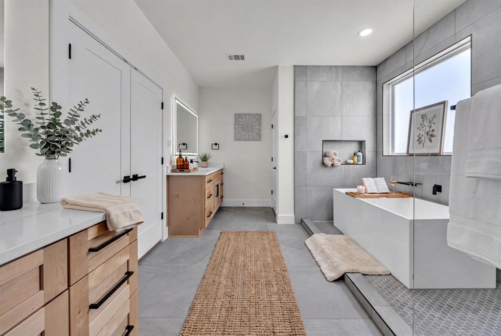 Bathroom featuring light wood-finish cabinetry, white solid-surface countertops, large-format tile flooring, a freestanding rectangular soaking tub, and a glass-enclosed shower area with a built-in recessed wall niche