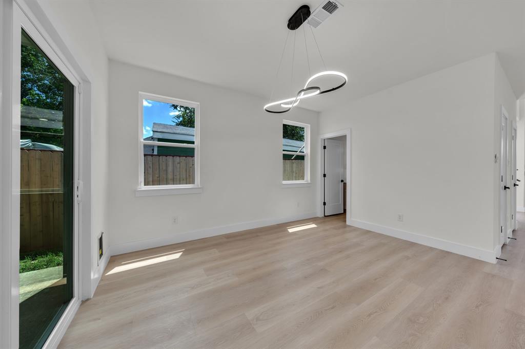 Light-filled room featuring wood-finish flooring, white walls, double-pane windows, a sliding glass door, and a modern circular LED pendant light fixture Light-filled room featuring wood-finish flooring, white walls, double-pane windows, a sliding glass door, and a modern circular LED pendant light fixture