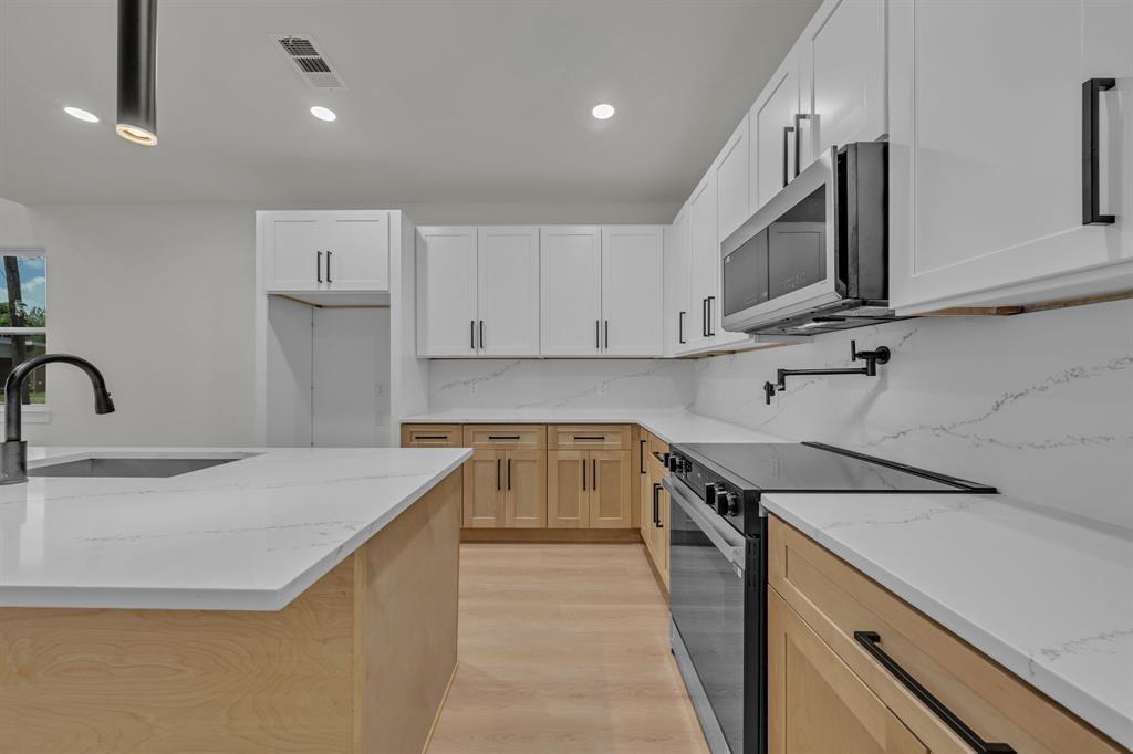 Kitchen featuring white upper cabinetry, natural wood-finish lower cabinetry, stone-surface countertops, a matching stone-surface backsplash, and a built-in pot filler faucet Kitchen featuring white upper cabinetry, natural wood-finish lower cabinetry, stone-surface countertops, a matching stone-surface backsplash, and a built-in pot filler faucet