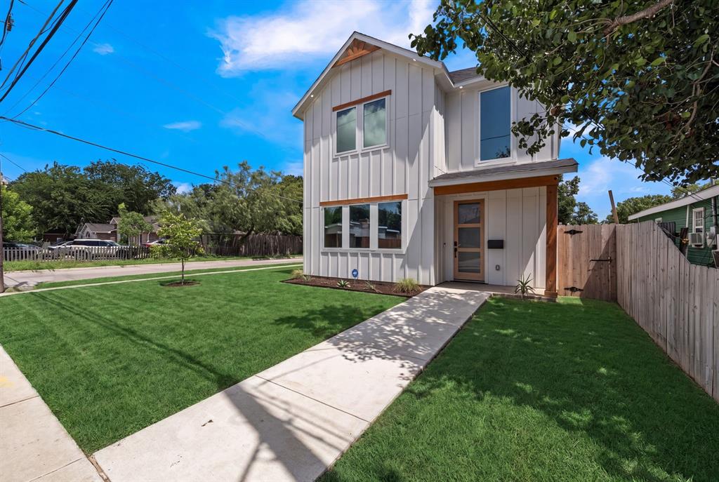 Two-story vertical siding exterior with wood-tone trim, expansive front lawn, paved walkway, and modern entry door with glass paneling