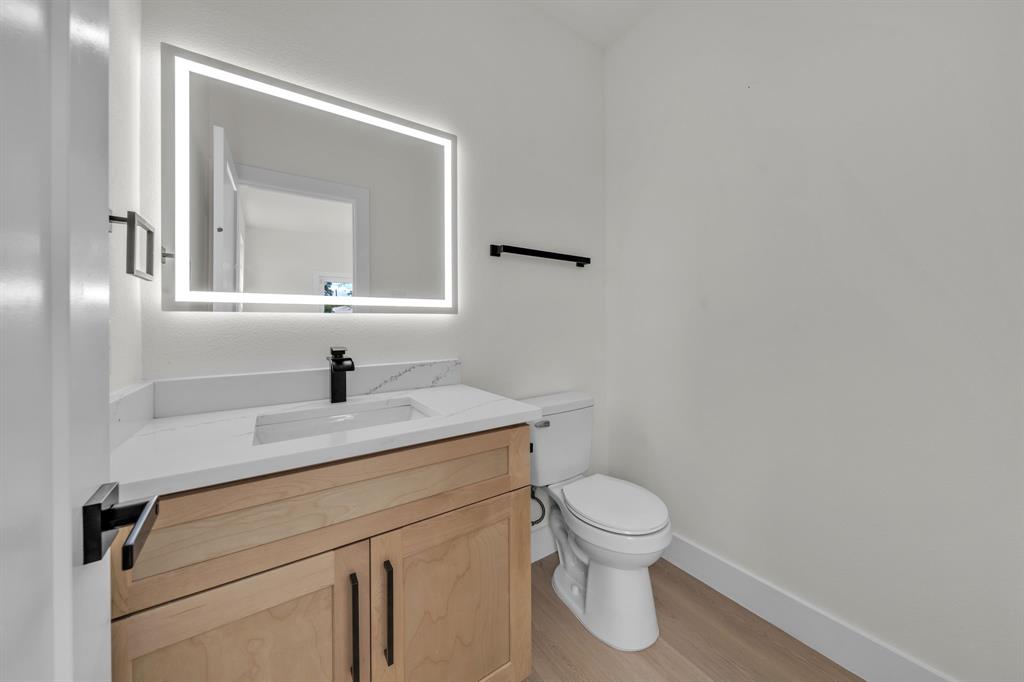 Wood-finish vanity with a rectangular sink, white countertop, matte black faucet, and rectangular LED-backlit mirror