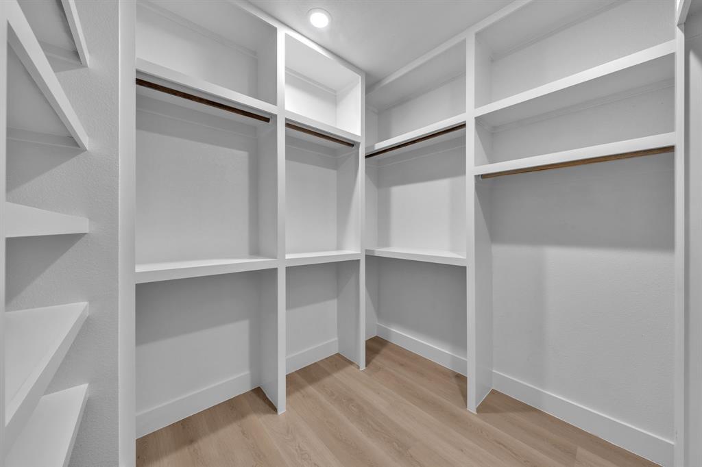 Custom walk-in closet featuring extensive built-in white shelving, integrated hanging rods, and wood-finish flooring