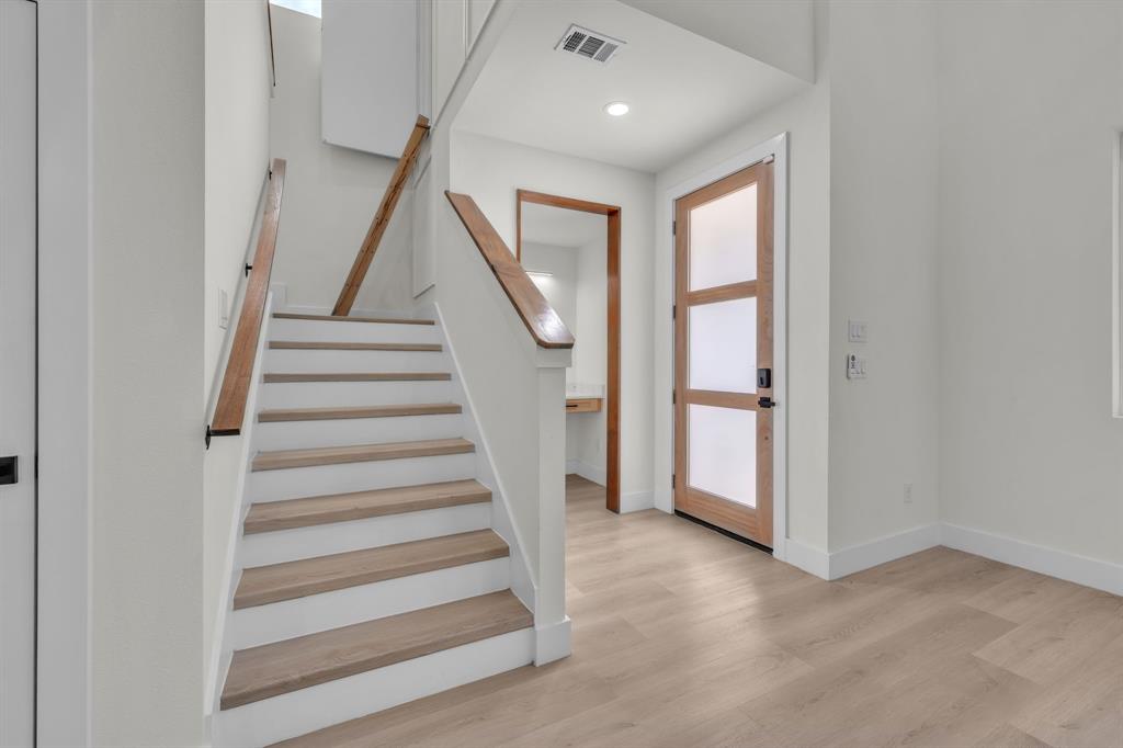 Entryway featuring a front door with glass panels, wood-finish flooring, and a staircase with wood handrails and wood-tread stairs