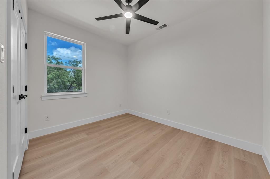 Neutral-toned room featuring wood-finish flooring, a matte black multi-blade ceiling fan with integrated lighting, and a double-door closet with black hardware