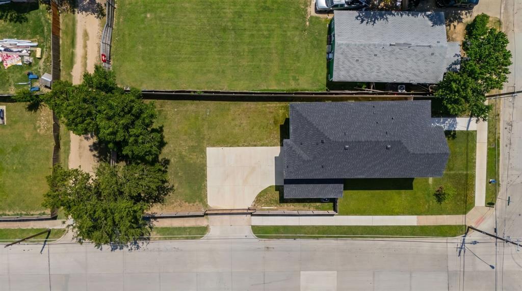 Aerial perspective of a corner lot featuring a concrete driveway, mature trees, expansive lawn space, and a dark-toned asphalt shingle roof