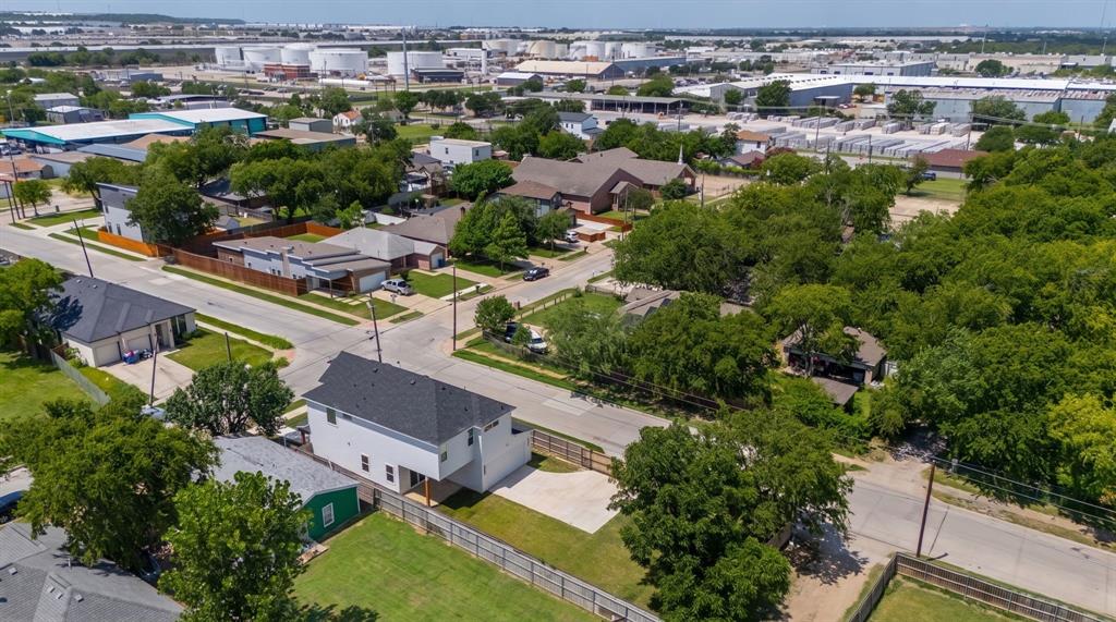 Aerial view of a multi-level residence featuring a dark shingle roof, white exterior siding, concrete driveway, and a wood privacy fence