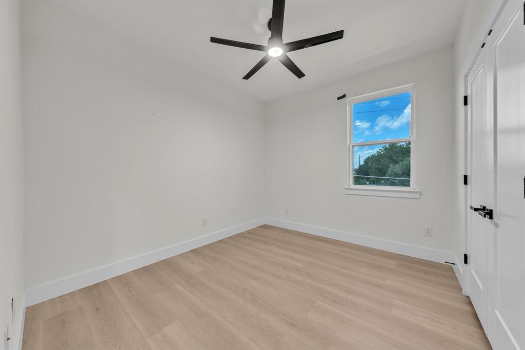 Interior space featuring wood-finish flooring, a matte black multi-blade ceiling fan with integrated lighting, a single-hung window, and a door with matte black hardware