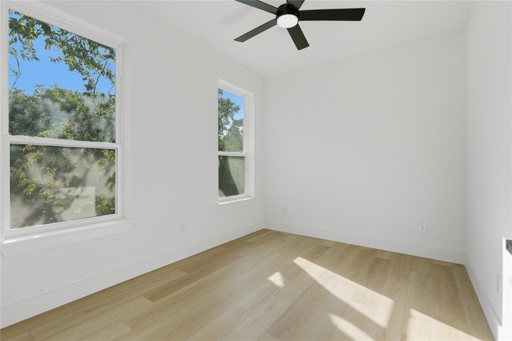 Neutral-toned room featuring wood-finish flooring, dual windows, and a matte black ceiling fan with an integrated light fixture