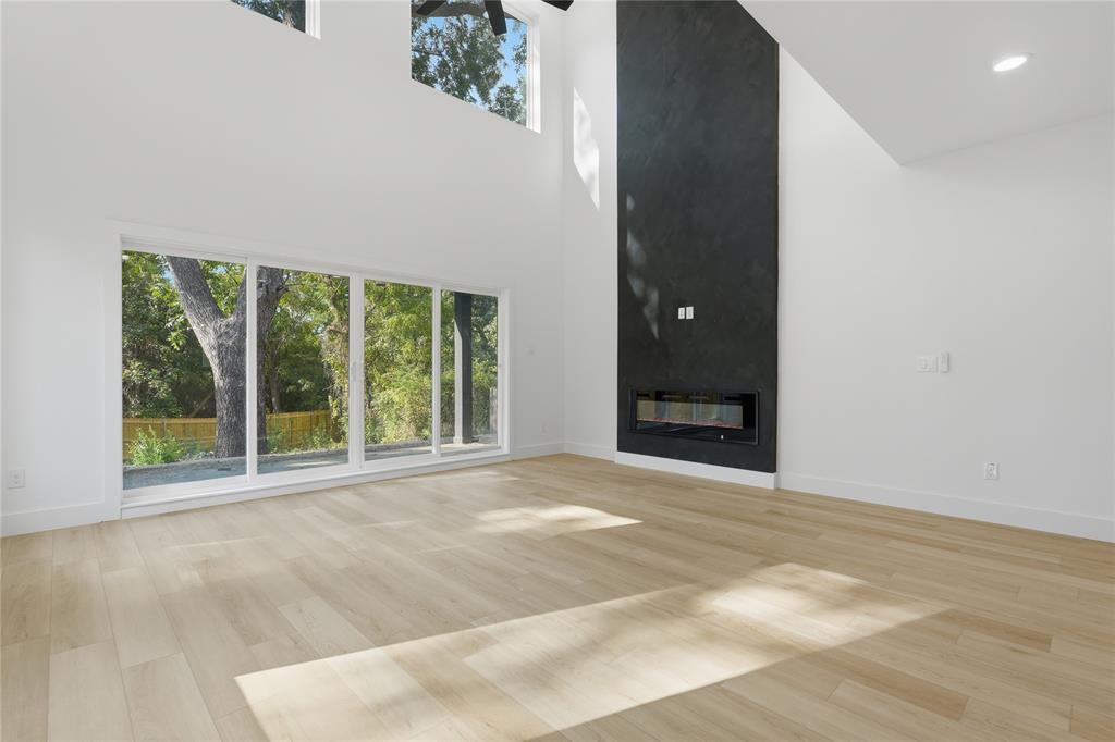 Double-height ceiling featuring recessed lighting and multi-level windows, floor-to-ceiling dark stone-finish fireplace surround with integrated linear electric insert, and wide-plank wood-finish flooring