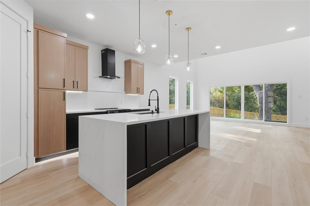 Kitchen featuring a waterfall-edge island with solid-surface countertops, two-tone custom cabinetry, a matte black gooseneck faucet, and light-toned wood-finish flooring