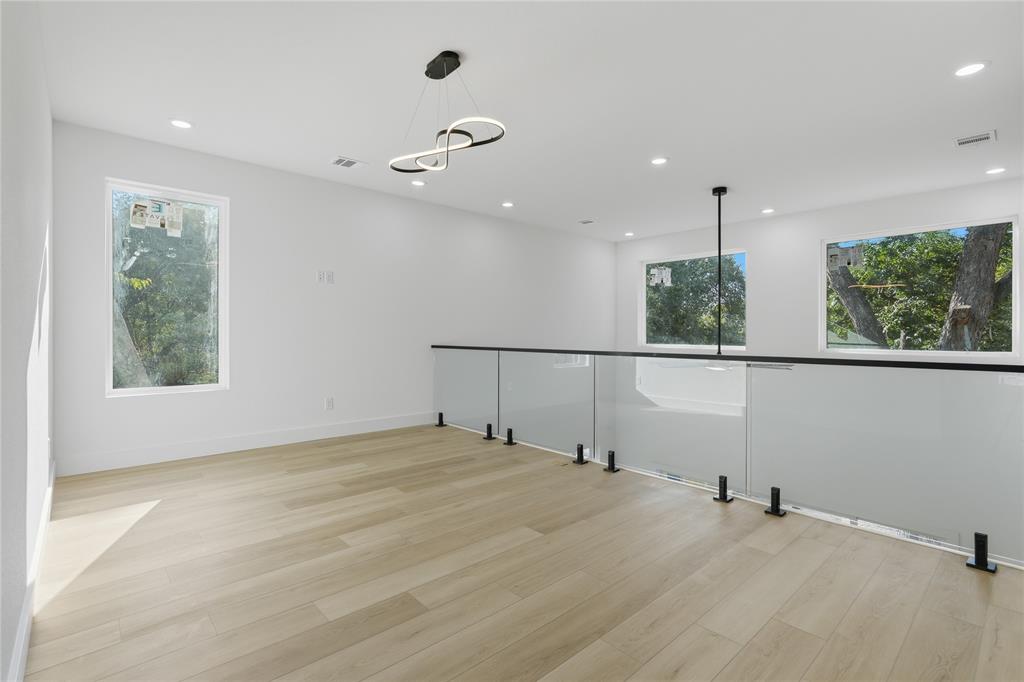 Open-concept interior featuring wood-finish flooring, recessed lighting, a contemporary looped chandelier, and a glass panel railing system with matte black hardware