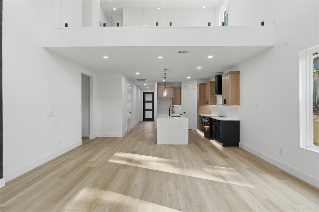Open-concept interior featuring wood-finish flooring, a kitchen island with a quartz countertop, dual-tone cabinetry, recessed lighting, and a glass-paneled mezzanine railing