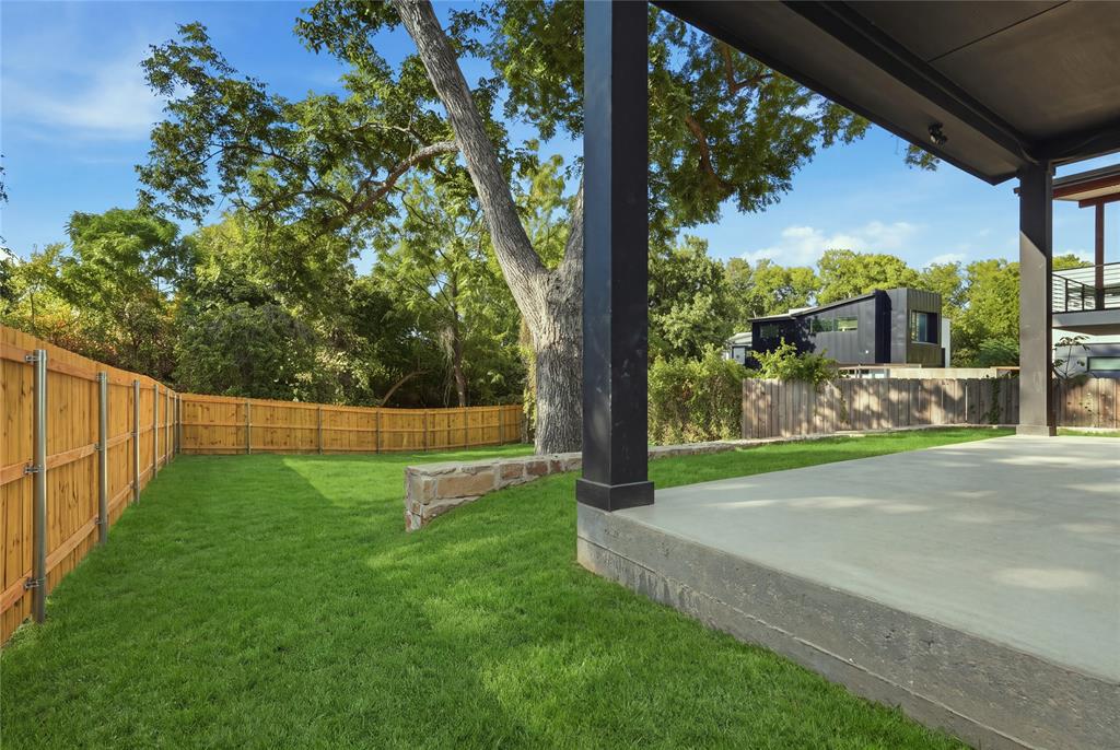 Covered patio featuring a concrete slab foundation, horizontal wood fencing, natural stone retaining wall, and mature trees