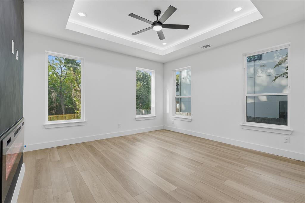 Tray ceiling featuring recessed lighting, wood-finish flooring, wall-mounted electric fireplace with a dark surround, and multiple energy-efficient windows