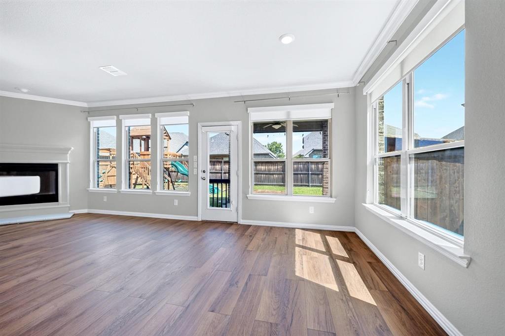 Open-concept room featuring wood-finish flooring, crown molding, multiple large windows, and a fireplace with a white mantle