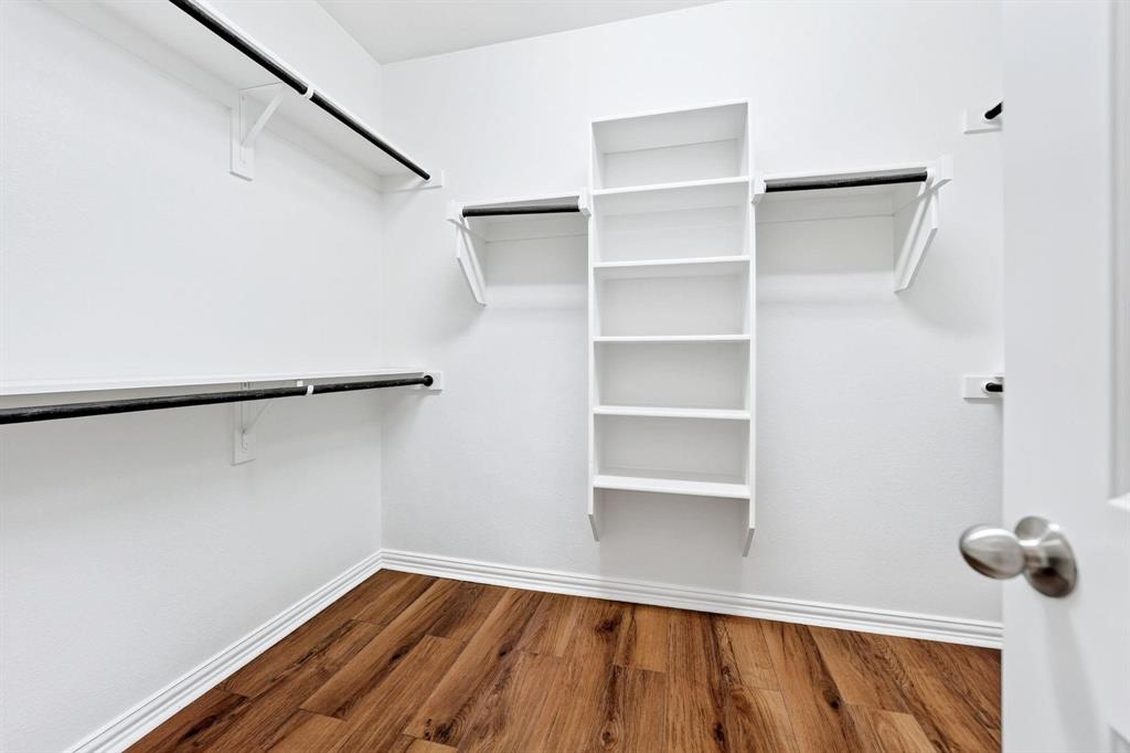 Walk-in closet featuring wood-finish flooring, white shelving units, and multiple metal hanging rods