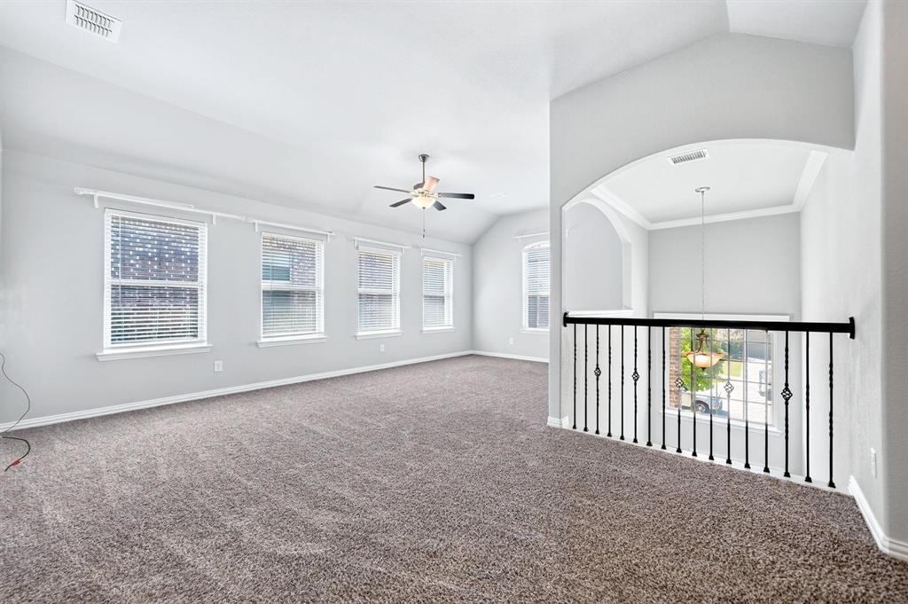 Vaulted ceilings, carpeting, black metal baluster railing, archway, and multiple windows