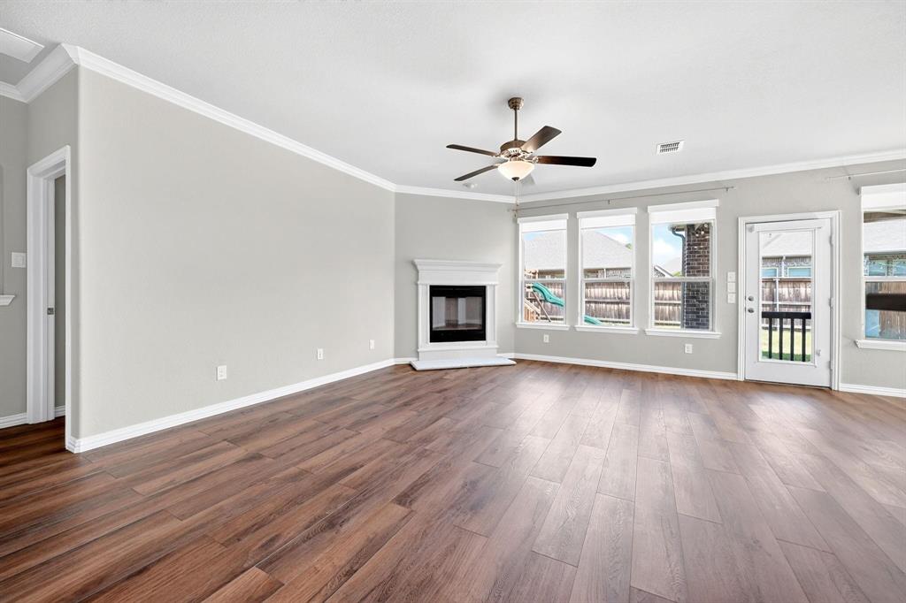 Wood-finish flooring, corner fireplace with a mantel, ceiling fan with integrated lighting, and multiple windows providing natural light
