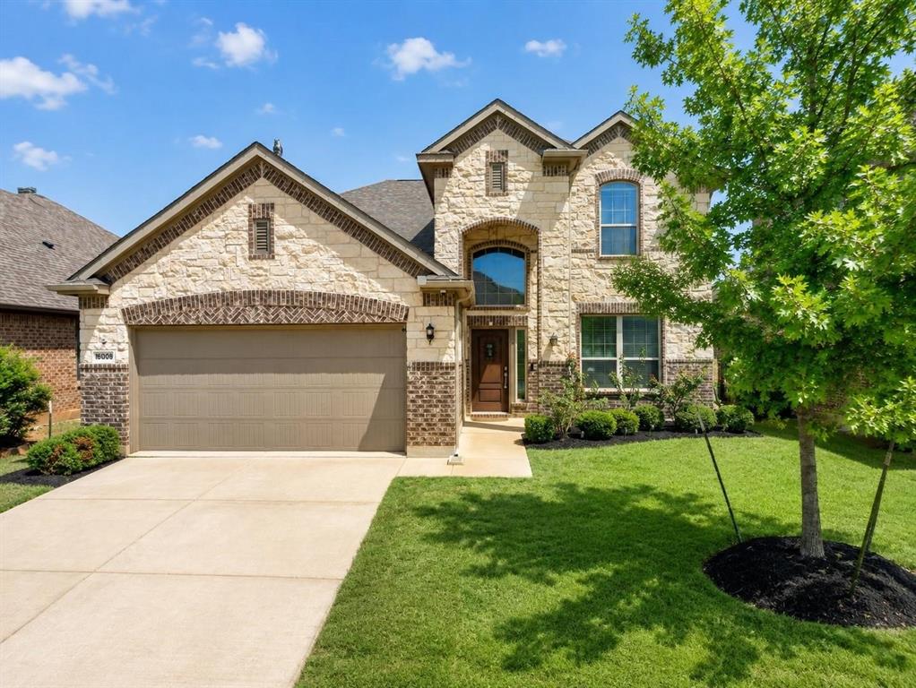 Two-story exterior featuring light-toned stone masonry, brick accents, a gabled roofline, an arched entryway, and a concrete driveway