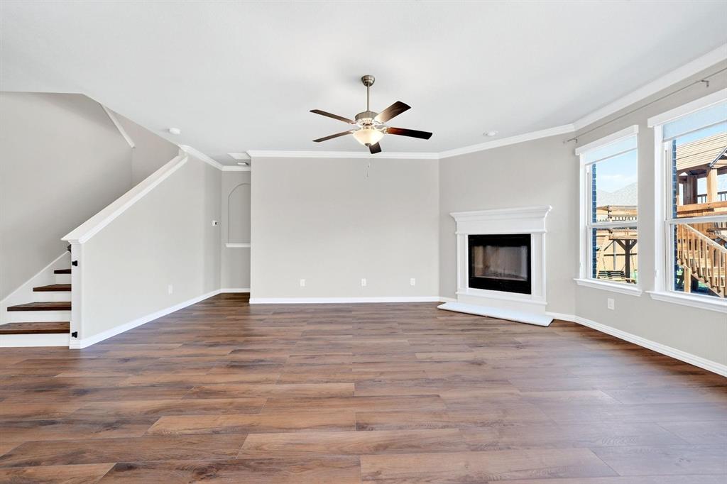 Open floor plan featuring wood-finish flooring, a fireplace with a white mantel, crown molding, and a ceiling fan