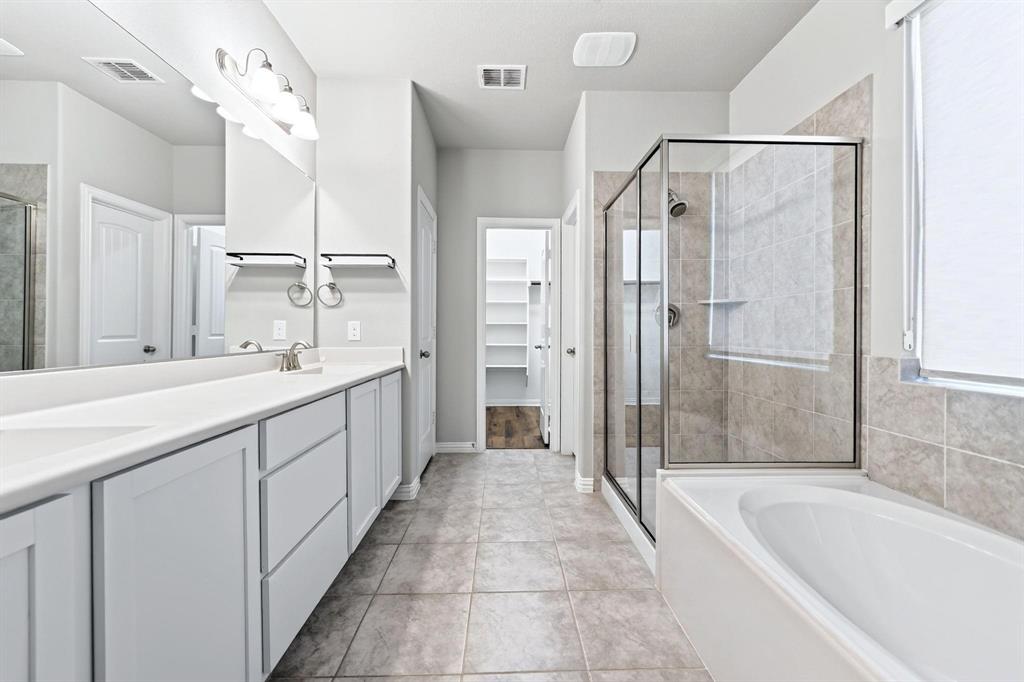 Bathroom featuring a dual-sink vanity with white cabinetry, a glass-enclosed shower, a soaking tub, and tile flooring