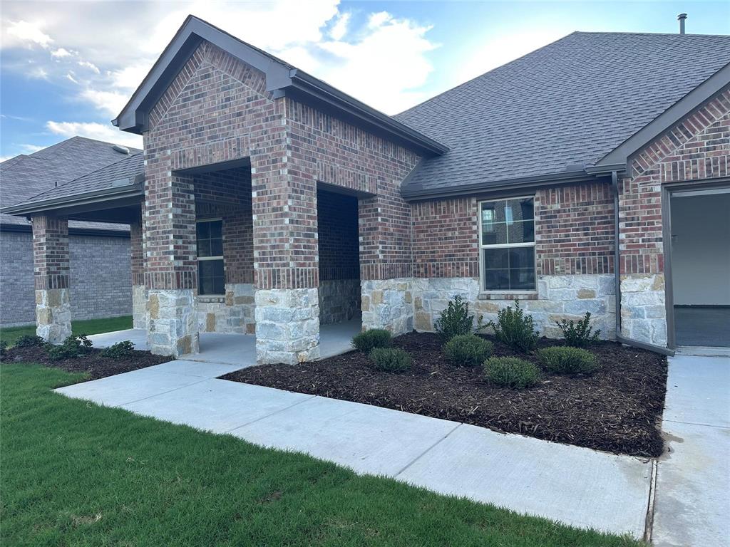 View of front facade with a shingled roof, brick siding, a front lawn, and stone siding