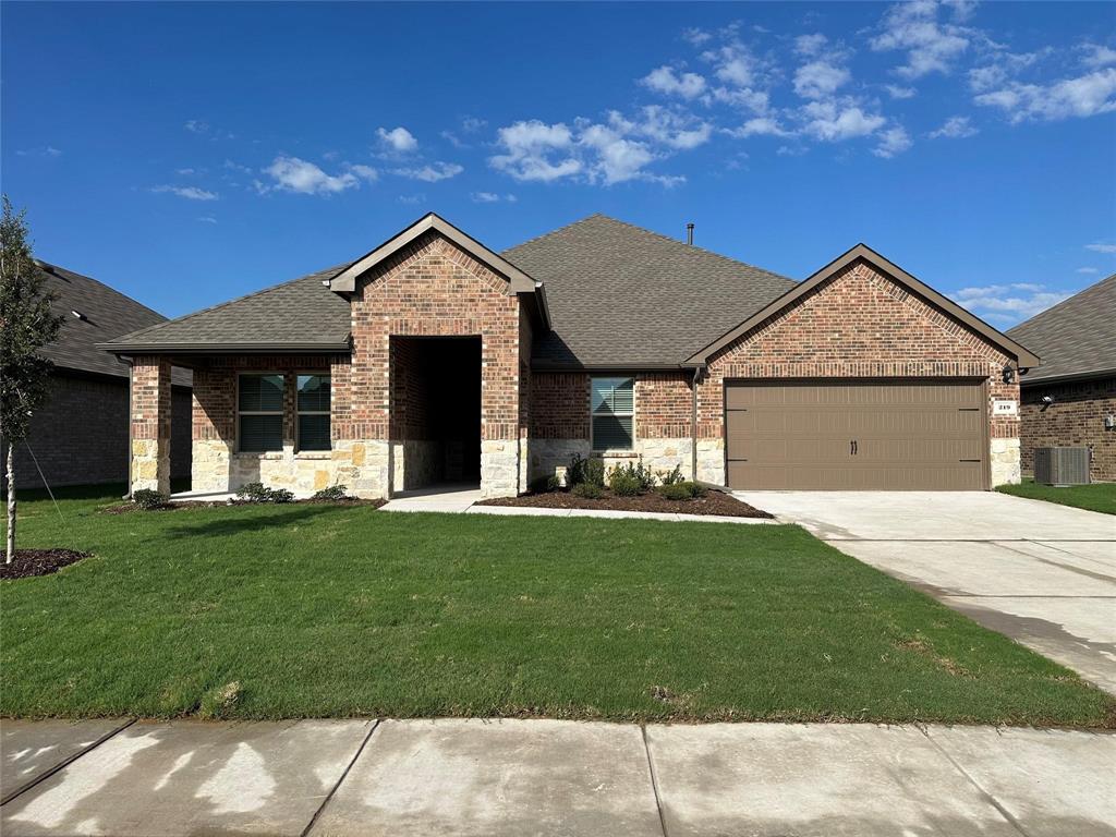 View of front of property with brick siding, a shingled roof, stone siding, and a front yard