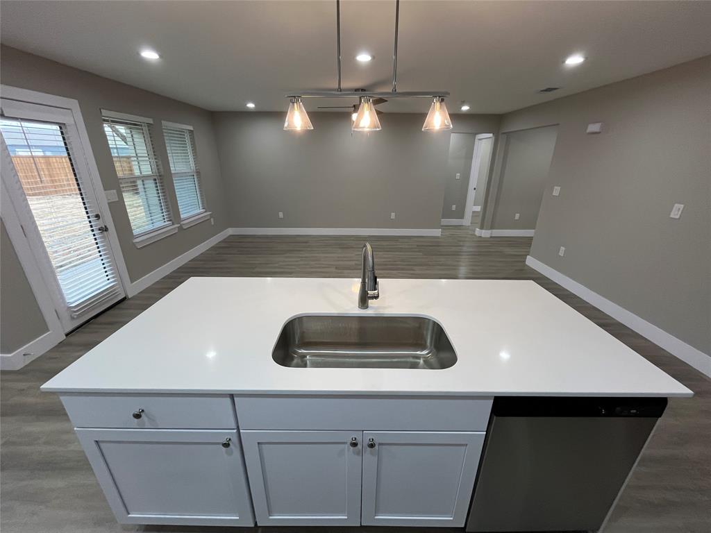 Kitchen island featuring solid-surface countertops, an undermount stainless steel sink, wood-finish flooring, and a three-light pendant fixture Kitchen island featuring solid-surface countertops, an undermount stainless steel sink, wood-finish flooring, and a three-light pendant fixture