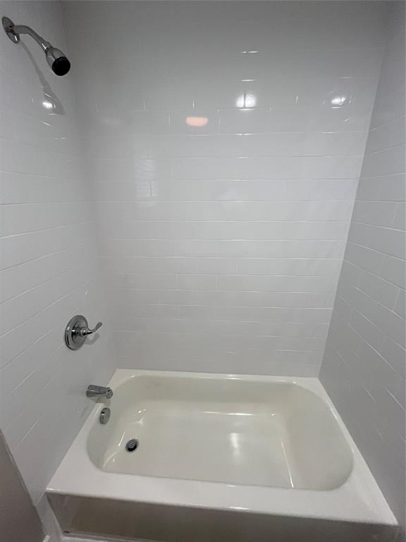 Bathtub enclosure featuring white subway tile surround, polished chrome shower head, single-handle pressure-balance valve, and matching chrome tub spout