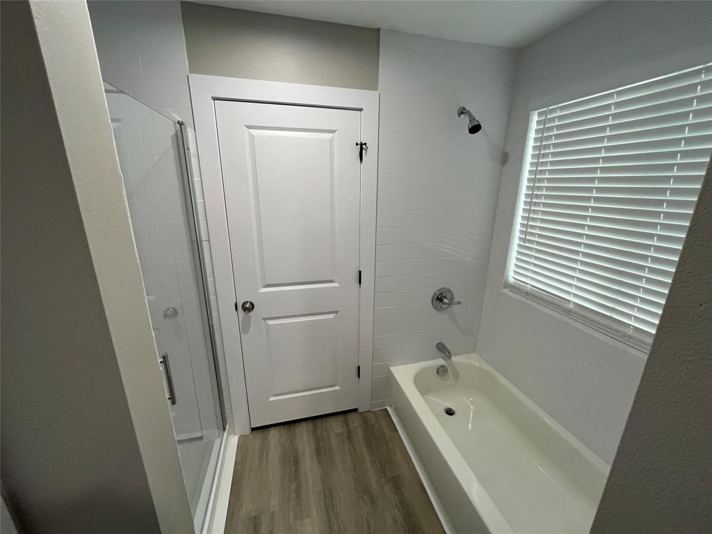 Bathroom featuring a glass-enclosed shower, integrated soaking tub with chrome fixtures, subway tile surround, and wood-finish flooring