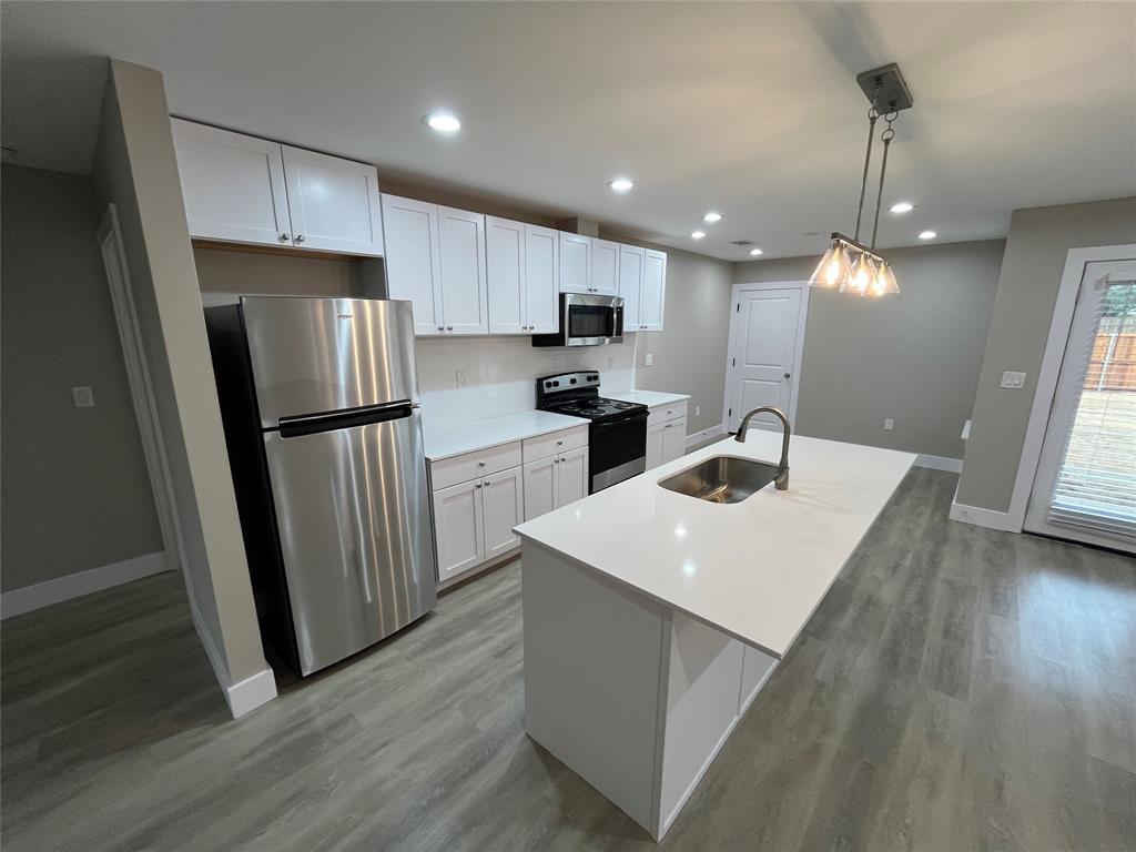 Kitchen featuring white shaker-style cabinetry, a central island with a solid-surface countertop, stainless steel appliances, and wood-finish flooring Kitchen featuring white shaker-style cabinetry, a central island with a solid-surface countertop, stainless steel appliances, and wood-finish flooring