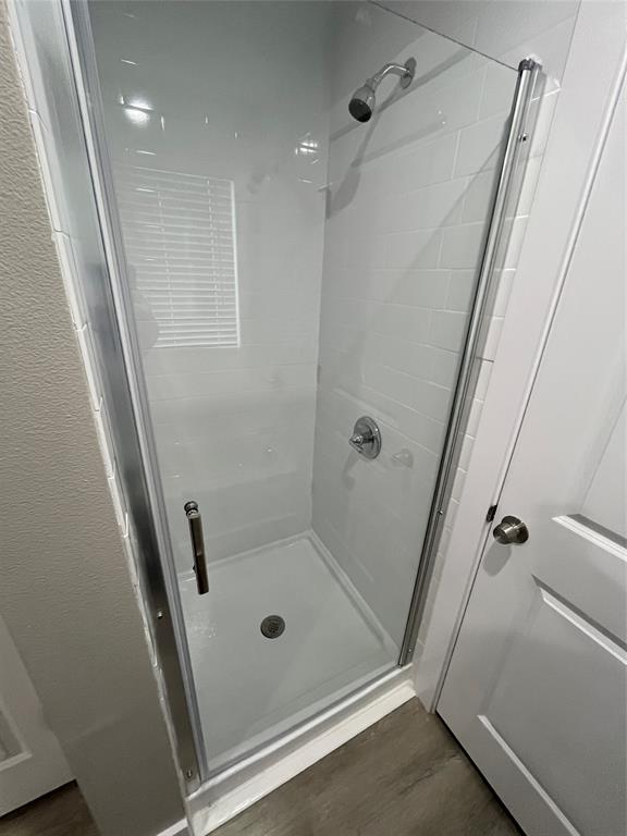 Walk-in shower featuring white subway-style wall tiling, a glass door with a metal frame, a chrome shower head, and a chrome pressure-balance valve