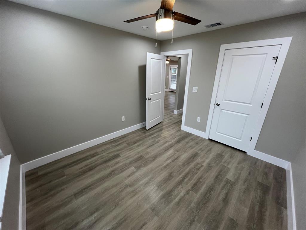 Room featuring wood-finish flooring, neutral wall paint, white two-panel doors, and a ceiling-mounted light fixture with a fan