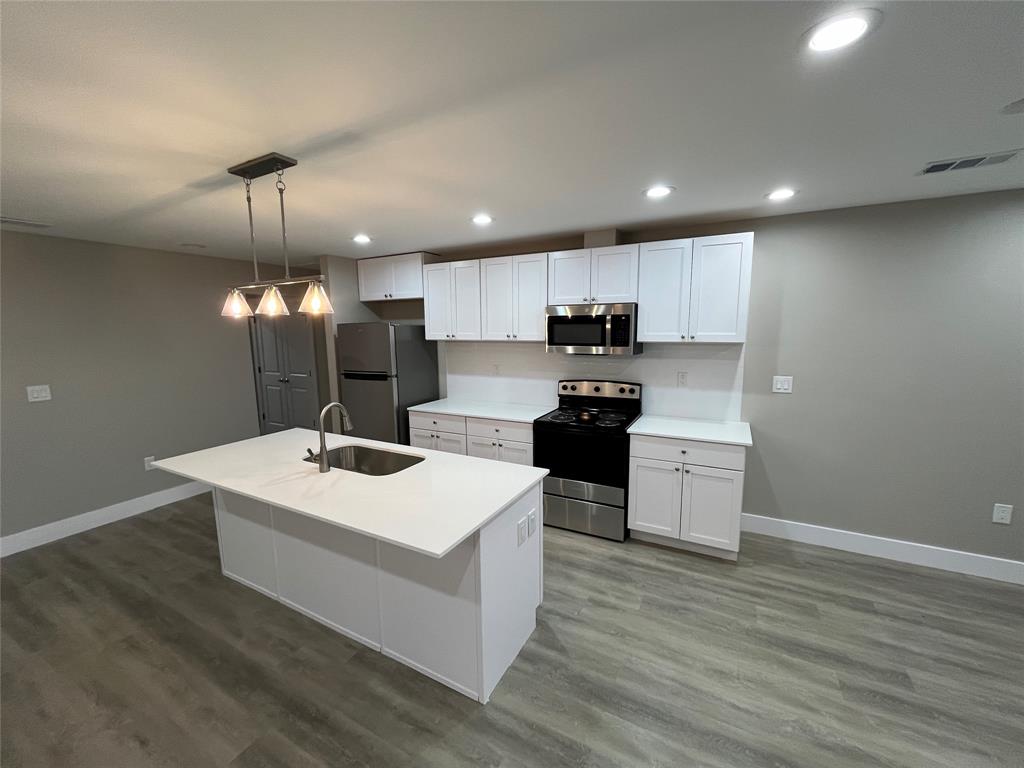 Kitchen featuring white cabinetry, quartz countertops, a central island with an integrated stainless steel sink, recessed ceiling lighting, and wood-finish flooring Kitchen featuring white cabinetry, quartz countertops, a central island with an integrated stainless steel sink, recessed ceiling lighting, and wood-finish flooring