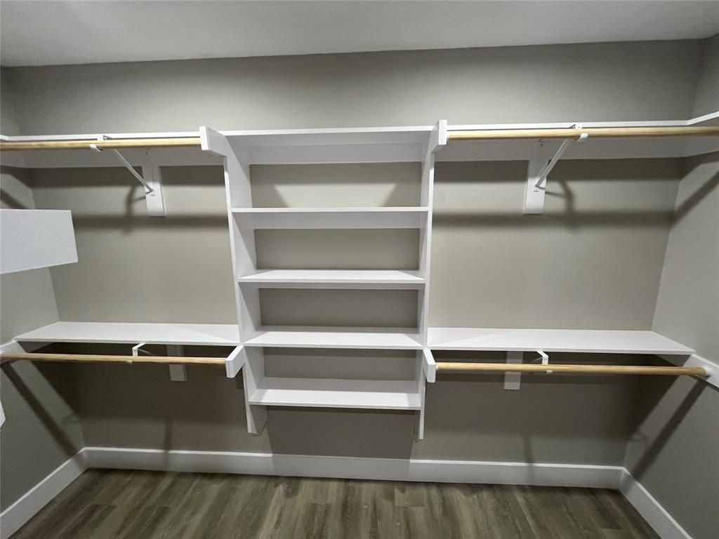 Walk-in closet featuring white built-in shelving, multi-level clothing rods, and wood-finish flooring