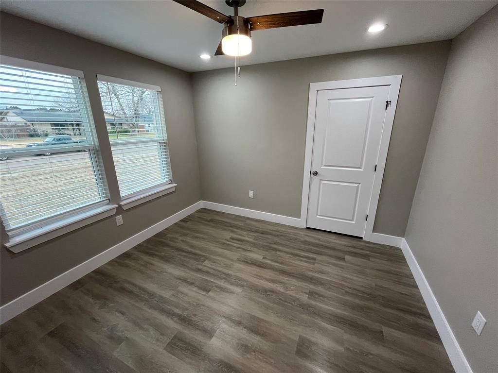 Neutral-toned interior space featuring wood-finish flooring, dual windows with integrated blinds, a modern ceiling fan with light fixture, and a white two-panel door