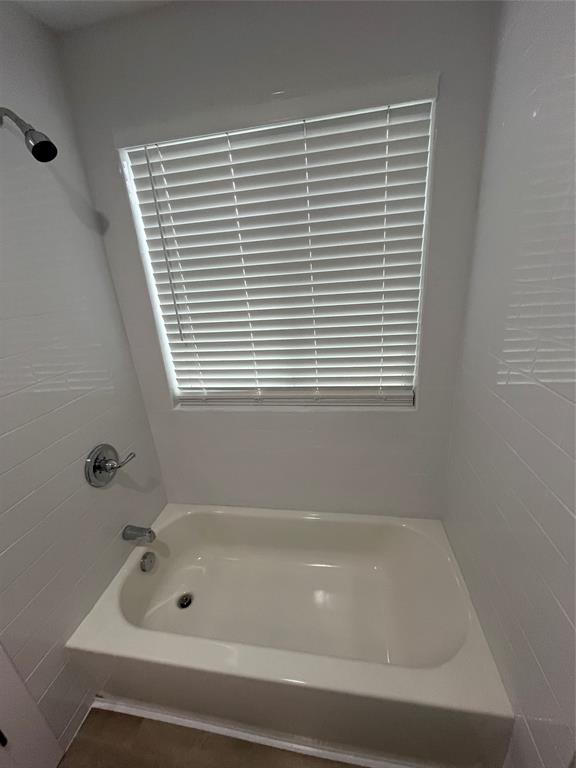 Bathtub surround featuring white wall tiling, polished chrome fixtures, and a recessed window with horizontal blinds