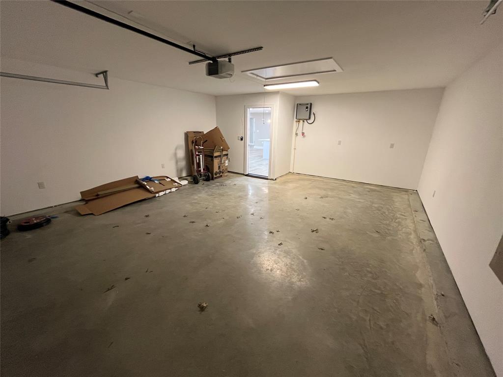 Attached garage featuring concrete flooring, an automated overhead door opener, ceiling-mounted light fixture, and interior access point with a designated electrical panel