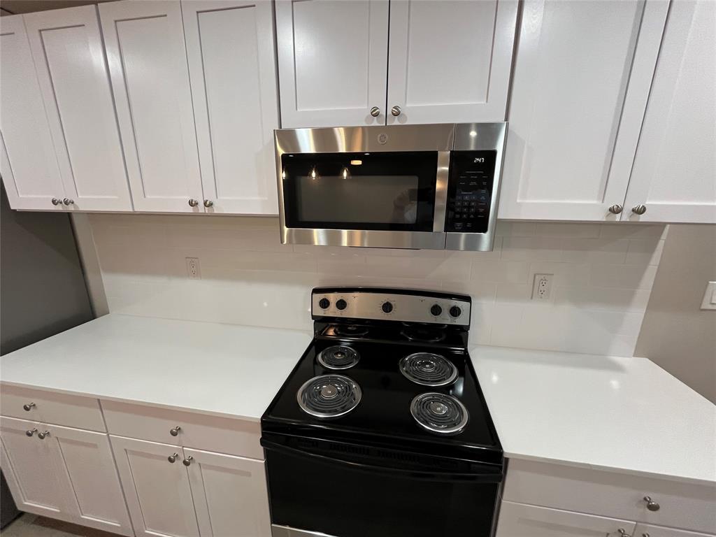 White Shaker-style cabinetry, solid-surface countertops, subway tile backsplash, stainless steel microwave, and electric range White Shaker-style cabinetry, solid-surface countertops, subway tile backsplash, stainless steel microwave, and electric range
