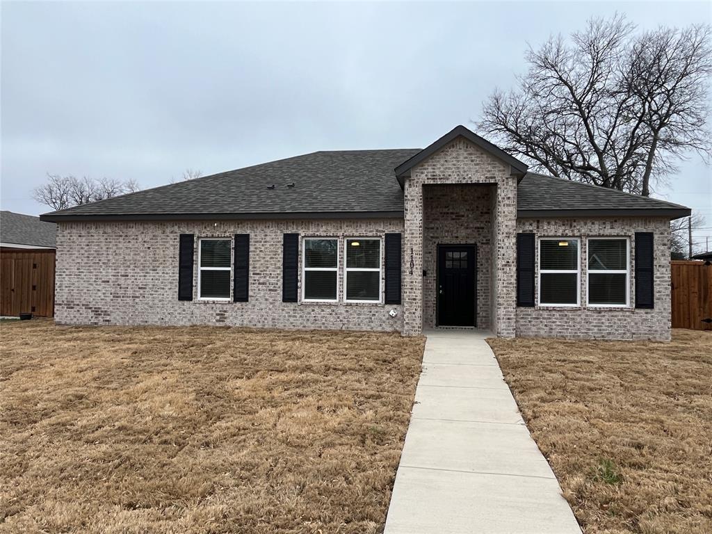 Single-story brick exterior featuring a prominent gabled entryway, dark-toned shutters, a multi-pane glass-inlay front door, and a concrete walkway