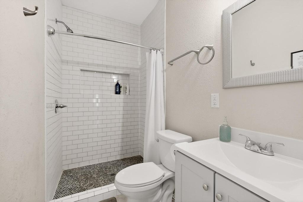 Bathroom featuring white subway tile shower surround, built-in shower niche, pebble-style floor tiling, light grey vanity with integrated sink, and polished chrome fixtures
