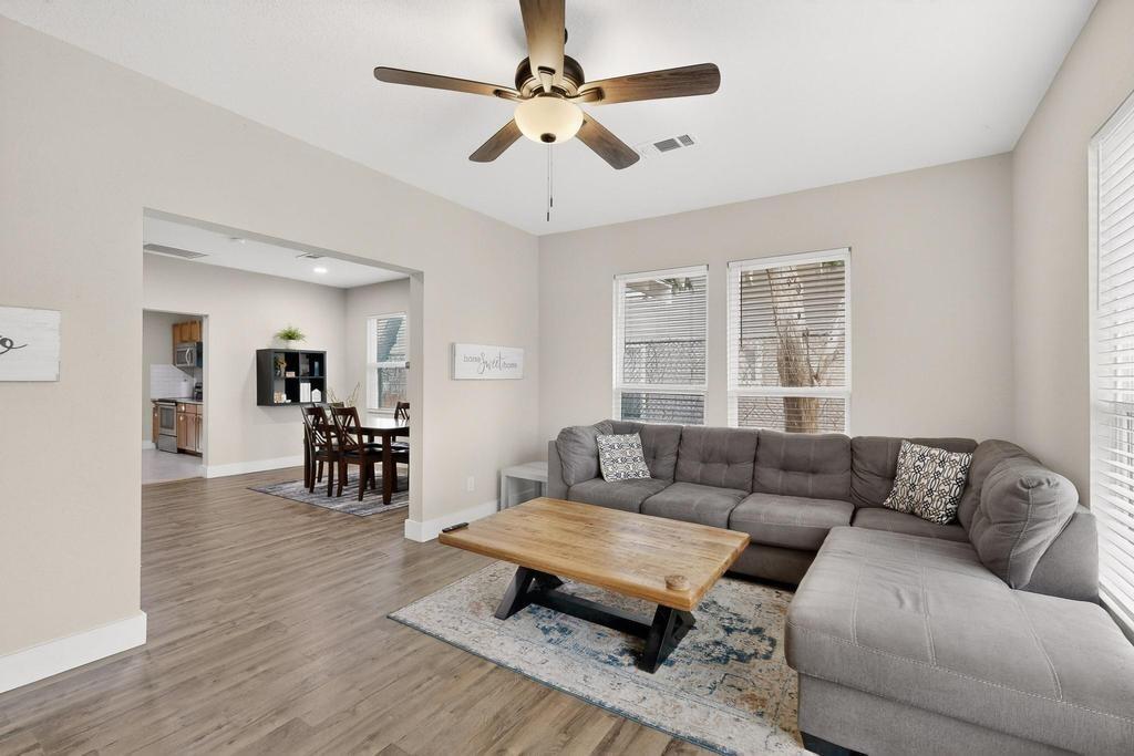Living area featuring wood-finish flooring, a ceiling fan with integrated lighting, and multiple windows with horizontal blinds