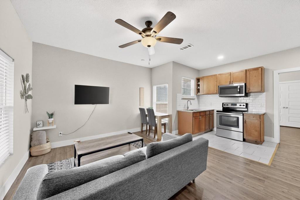 Kitchen featuring wood-finish cabinetry, stainless steel appliances, and subway tile backsplash, complemented by wood-finish flooring and a multi-blade ceiling fan