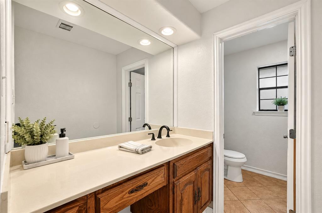 Bathroom vanity featuring a light-toned solid surface countertop, wood cabinetry, oil-rubbed bronze faucet hardware, a recessed lighting fixture, and a large wall-mounted mirror