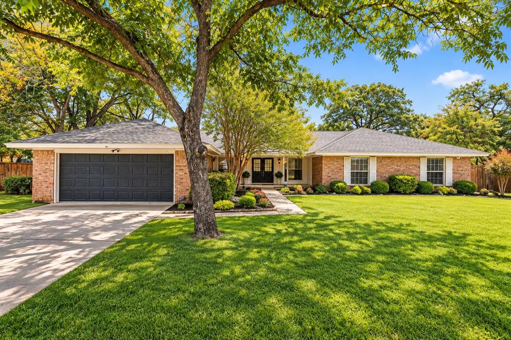 Single-story brick exterior featuring a multi-gabled roofline, double-door entryway, attached two-car garage, and mature landscape