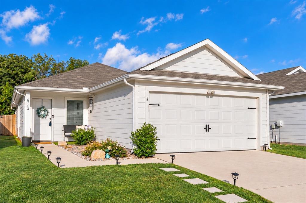 Single-story exterior featuring white horizontal siding, a gabled roofline, an attached two-car garage with decorative hardware, and a paved concrete driveway